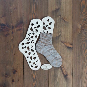 May include: Two white wooden sock blockers with a leaf pattern cut out. A beige and brown sock is stretched over one of the blockers. The blockers have the text "Made with &hearts; MiynJedrow" on them.