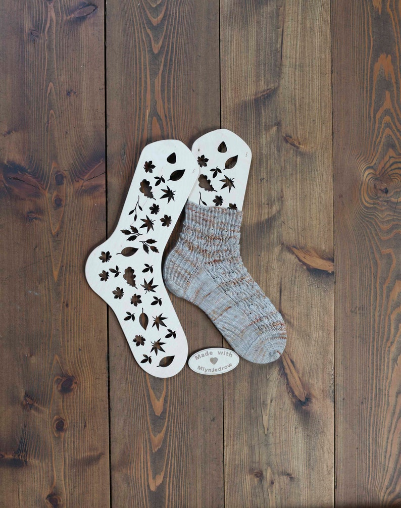 May include: Two white wooden sock blockers with a leaf pattern cut out. A beige and brown sock is stretched over one of the blockers. The blockers have the text "Made with &hearts; MiynJedrow" on them.