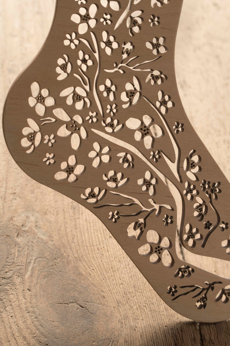May include: A wooden cutout of a foot with a floral design. The design features delicate flowers and branches, creating a intricate pattern.