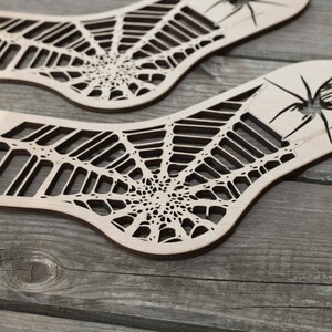 K&ouml;nnte beinhalten: Zwei Holzausschnitte eines Spinnennetzes mit einer Spinne in der Mitte. Die Ausschnitte sind aus hellbraunem Holz gefertigt und haben ein detailliertes Design.
