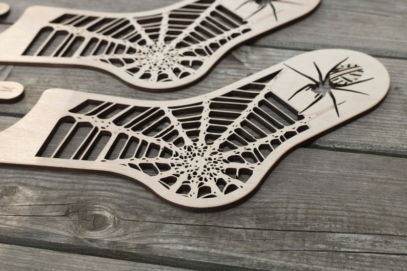 K&ouml;nnte beinhalten: Zwei Holzausschnitte eines Spinnennetzes mit einer Spinne in der Mitte. Die Ausschnitte sind aus hellbraunem Holz gefertigt und haben ein detailliertes Design.