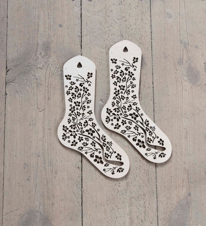 May include: Two white wooden sock-shaped forms with a floral pattern. The forms are designed to help knitters create socks.