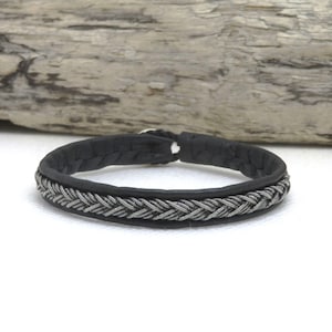 Puede incluir: Un brazalete de cuero negro con un diseño trenzado plateado.