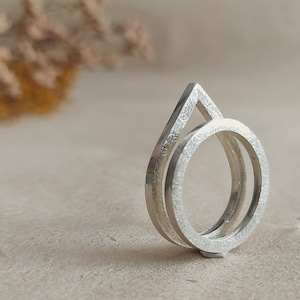 May include: A silver ring with a geometric design. The ring is made of two overlapping circles, one of which is shaped like a teardrop.