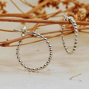 May include: A pair of silver hoop earrings with a beaded design. The earrings are small and delicate, and they would be a great addition to any jewelry collection.