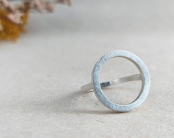 May include: A silver ring with a circle design. The ring is made of a smooth, brushed metal.