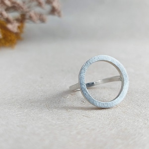 May include: A silver ring with a circle design. The ring is made of a smooth, brushed metal.