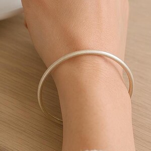 May include: A silver bangle bracelet on a person's wrist. The bracelet is simple and elegant, with a smooth, polished finish.
