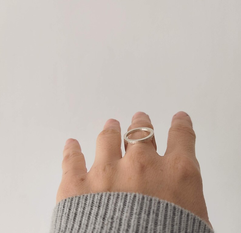 May include: A silver ring with a simple, circular design. The ring is worn on the middle finger of a hand.