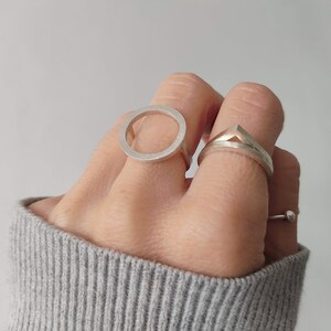 May include: Two silver rings on a hand. One ring is a simple circle, the other is a geometric shape with a pointed top.