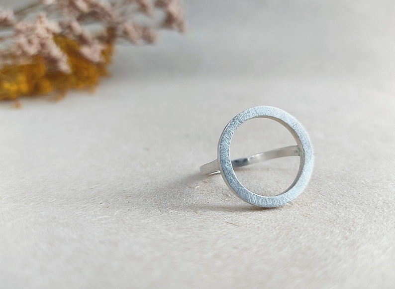 May include: A silver ring with a circle design. The ring is made of a smooth, brushed metal.