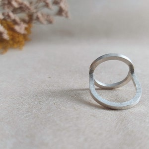 May include: A silver ring with a unique design featuring two interlocking circles. The ring is made of polished metal and has a smooth, modern look.