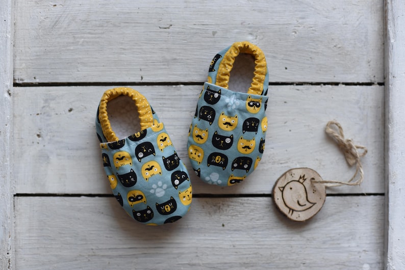 Peut inclure: Une paire de chaussons bleus pour b&eacute;b&eacute; avec une bordure jaune et un motif de chats noirs et jaunes.