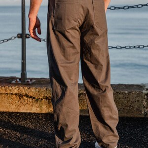 May include: Brown pants with a straight leg fit. The pants have two back pockets and two front pockets. The person is wearing white sneakers with a black Nike swoosh. The pants are made of a durable fabric and have a classic design.