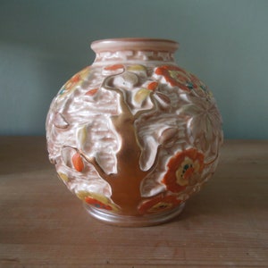 May include: A round ceramic vase with a textured surface and a gold tree design. The vase is decorated with orange, yellow, and green flowers.
