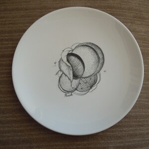 Peut inclure: Une assiette en céramique blanche avec un dessin en noir et blanc d'une pêche. Le dessin est stylisé et montre la pêche en coupe. Le mot "Pêche" est écrit sous le dessin.