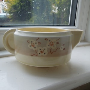 以下が含まれることがあります： 茶色の帯と花柄の白い陶器のクリーマー。花は白地に茶色の芯があり、茶色の枝に配置されています。