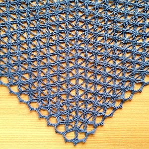 Può includere: Uno scialle triangolare all'uncinetto di colore blu con un intricato motivo a reticolo traforato. Il tessuto è realizzato con filato sottile, creando una griglia geometrica di forme a stella interconnesse che si restringono verso il basso.