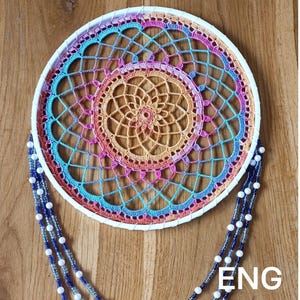 May include: A circular dream catcher featuring a white hoop with a multi-colored crochet web in shades of orange, pink, and blue. Three long strands of blue and clear beads interspersed with white pearls hang from the bottom. The text ENG is visible.