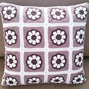 May include: A crocheted pillow with a brown and white floral pattern. The pillow is made of a soft, textured yarn and has a square shape.