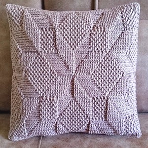 May include: A soft, light purple knitted cushion with a geometric pattern. The cushion is on a brown sofa.