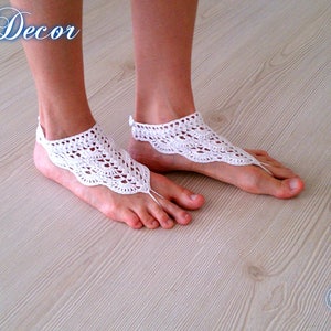 Pu&ograve; includere: Sandali a piedi nudi all'uncinetto bianchi con un design a bordo smerlato. I sandali sono indossati sui piedi, con un anello per le dita e un cinturino alla caviglia. L'immagine ha il testo "Knitted Decor" e "Pattern".