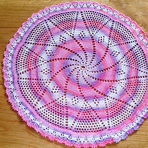 Puede incluir: Un tapete circular hecho a mano con un dise&ntilde;o en espiral. El tapete presenta una combinaci&oacute;n de hilos blancos, rosas y morados, creando un patr&oacute;n visualmente atractivo. Los bordes est&aacute;n acabados con un borde festoneado. Este art&iacute;culo decorativo es adecuado para la decoraci&oacute;n del hogar, aprox. 30 cm de di&aacute;metro.