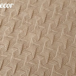 May include: A beige knitted blanket with a geometric chevron pattern. The blanket has a textured surface and is made of soft yarn. The words "Knitted Decor" and "Pattern" are visible in the image.
