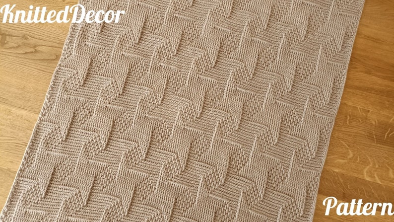 May include: A beige knitted blanket with a geometric chevron pattern. The blanket has a textured surface and is made of soft yarn. The words "Knitted Decor" and "Pattern" are visible in the image.
