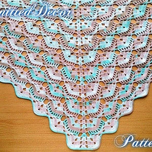 May include: A crocheted shawl with a delicate pattern in shades of white, pink, and blue. The shawl is triangular in shape and has a scalloped edge.