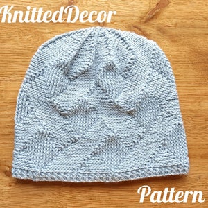 Op de afbeelding: Een lichtgrijze gebreide beanie met een textuurpatroon. De beanie ligt op een houten oppervlak. Knitted Decor Pattern.