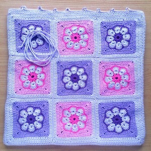 May include: A crocheted blanket with a repeating pattern of purple and pink flowers. The blanket is made of a soft, textured yarn and is perfect for adding a touch of handmade charm to any room.