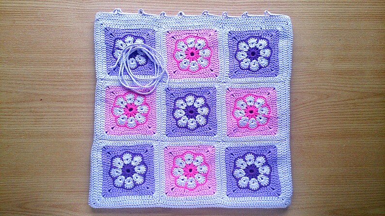 May include: A crocheted blanket with a repeating pattern of purple and pink flowers. The blanket is made of a soft, textured yarn and is perfect for adding a touch of handmade charm to any room.