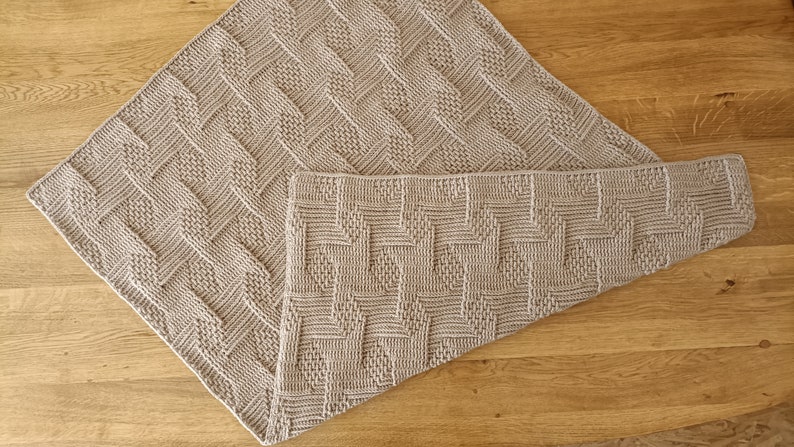 May include: Two light beige knitted blankets with a geometric pattern. One blanket is folded into a square, and the other is partially unfolded, revealing its rectangular shape. The blankets are made of a soft, textured material.