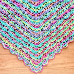 May include: A triangular crochet shawl featuring a repeating fan stitch pattern in a vibrant gradient of colours including bright pink, turquoise, lime green, and purple, finished with a scalloped edge along the bottom border of the textile.