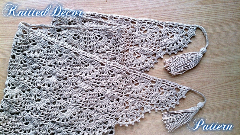 May include: A beige, knitted decor item with a delicate, openwork pattern. The item has a scalloped edge and is finished with tassels at each end. The text "Knitted Decor" and "Pattern" are visible in the image.