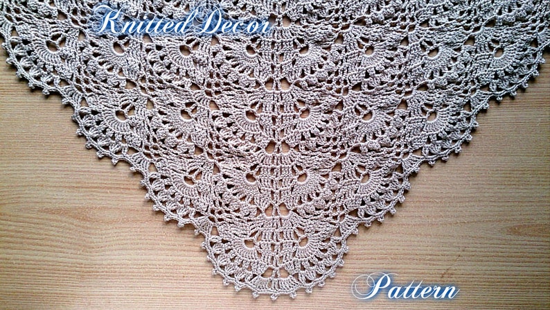 May include: A beige, crocheted shawl with a detailed, openwork pattern. The shawl is triangular, with a scalloped edge. The words "Knitted Decor" and "Pattern" are written on the image.