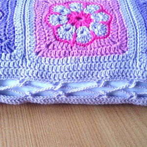 May include: A crocheted pillow with a purple, pink, and white floral design. The pillow has a white inner lining and a crocheted border.