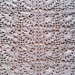 May include: Close-up of a crocheted textile with a repeating floral pattern. The handmade piece is in a neutral, light gray color, with a delicate, openwork design. The texture is soft and intricate, suitable for a shawl or blanket.