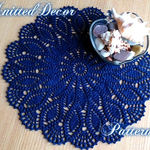 May include: A navy blue crocheted doily with a delicate pattern. The doily is on a wooden surface and has a bowl of seashells in the center.