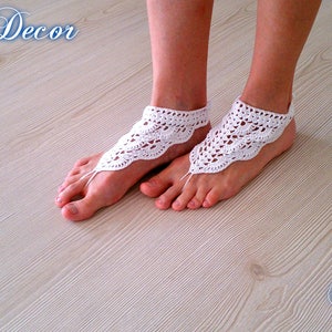 Pu&ograve; includere: Sandali a piedi nudi all'uncinetto bianchi con un delicato design traforato. I sandali sono indossati a piedi nudi, con un anello per le dita e un cinturino alla caviglia. Il testo "Knitted Decor" e "Pattern" &egrave; incluso.