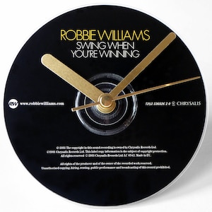 May include: A black vinyl record clock featuring Robbie Williams's album "Swing When You're Winning". The clock has gold hands and a black face with white text.