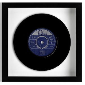 Op de afbeelding: Een zwarte 45 toeren vinylplaat ingelijst in een vierkante zwarte lijst. Het centrale label is blauw met zilverkleurige tekst, voorzien van het Fontana-logo, de titel Wild Thing, de artiest The Troggs, een 45 toeren aanduiding en mono label.