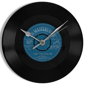 May include: A black vinyl record clock with silver hands. The clock face features a blue label with the text "I CAN'T STOP LOVING YOU" and "Ray Charles". The clock is a unique decorative item.