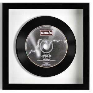 May include: A black framed CD single with a black and silver CD featuring the band Oasis. The CD has the song titles "Wonderwall", "Round Are Way", "The Swamp Song", and "The Master Plan".