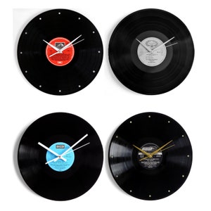 May include: Four vinyl record clocks with different colored labels and clock hands. The clocks are all black and have white numbers around the edge.