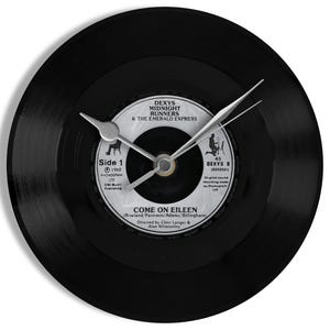 May include: A black vinyl record clock with silver hands. The clock face displays the label of a record by Dexys Midnight Runners, with the song title "Come On Eileen" clearly visible.