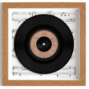 Op de afbeelding: Een ingelijste 45 RPM vinylplaat met het nummer "Dreadlock Holiday" van 10cc. De plaat wordt getoond op een blad met muziek.