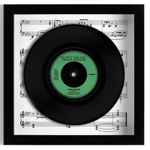 May include: A black vinyl record with a green label. The label features the text "ROXY MUSIC" and "MORE THAN THIS". The record is framed against a sheet of music.