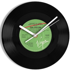 May include: A black vinyl record clock with white clock hands. The clock face is a green label with the text "AGAINST ALL ODDS" and "PHIL COLLINS". The clock is a unique decorative item.